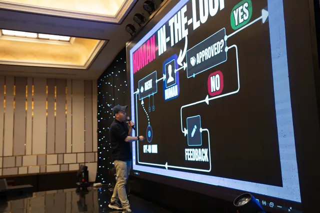 Daniel Nguyen on stage pointing at a human-in-the-loop workflow diagram on a large screen at the n8n meetup