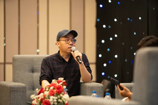 Daniel seated on a panel with a microphone in front of a starlit backdrop